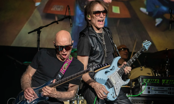 Bandmates from SATCHVAI clutch their guitars and perform on stage.