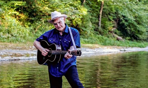 Verlon Thompson playing guitar while standing in a shallow river