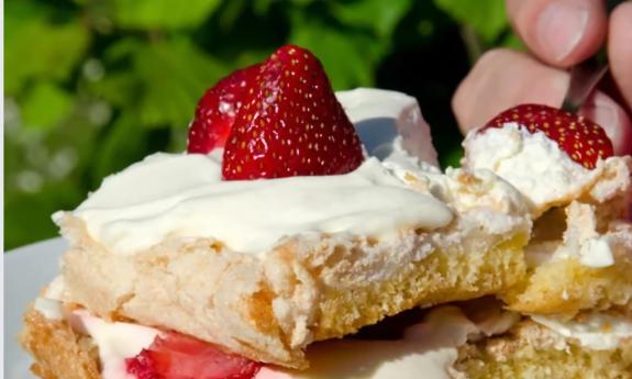 A plate of strawberry shortcake, and a hand holding a forkful of the dessert