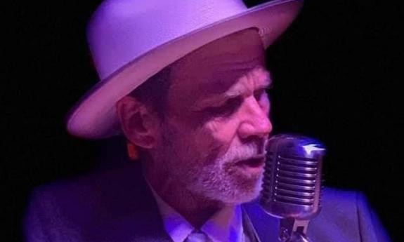 Beau Knott at the microphone, at night, in white brim hat