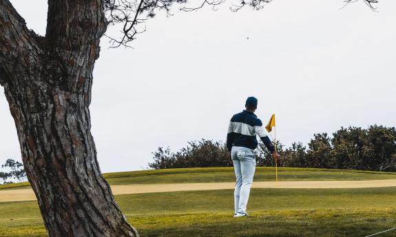 A golfer, seen from the back, as he is facing a green with a yellow-flagged hole