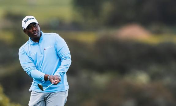 A golfer in a blue jersey in the middle of a chip shot