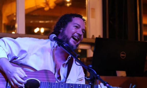 Musician John Fowler onstage playing his guitar and laughing.