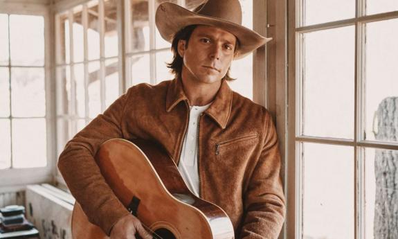 Lukas Nelson poses with a brown jacket and matching guitar.