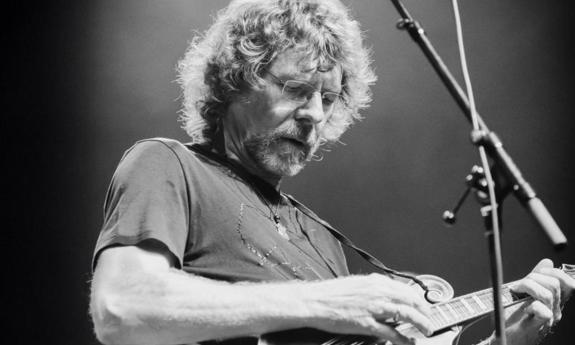 Sam Bush clutches his guitar and performs on stage. 