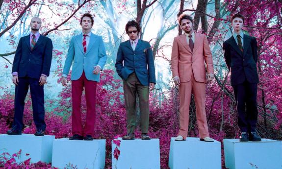 Members of Tripping Daisy suit up and pose beneath trees adorned with pink leaves.