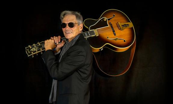 Russ DeFilippis with his guitar over his shoulder, wearing black