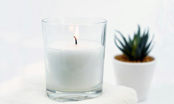 A candle on a white towel with a small plant in the background