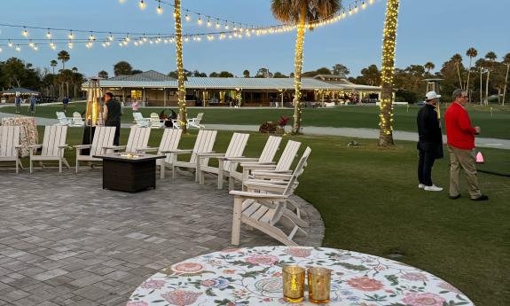 Seating on a stone patio, strung with overhead lights, and warmed by a fire pit