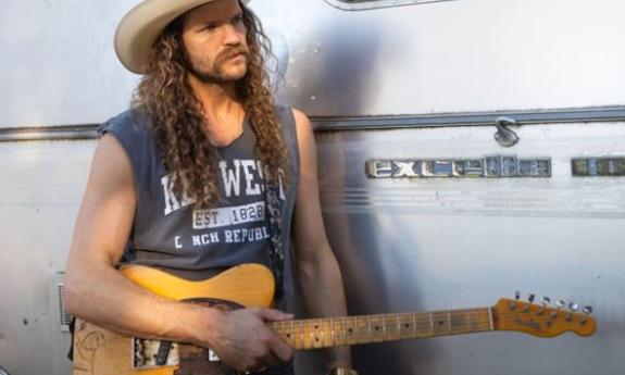 Andy Thomas wears a cowboy hat and poses with his guitar.