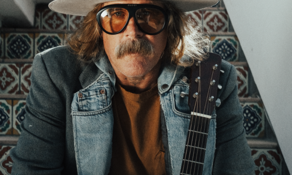 Donavon Frankenreiter sits on a staircase and poses with his guitar. 