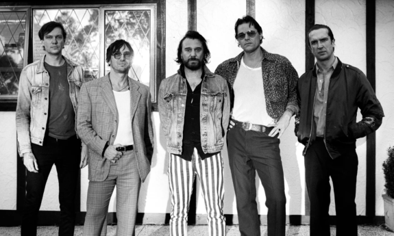 Bandmates from Jet pose in front of a wall with picture frames. 