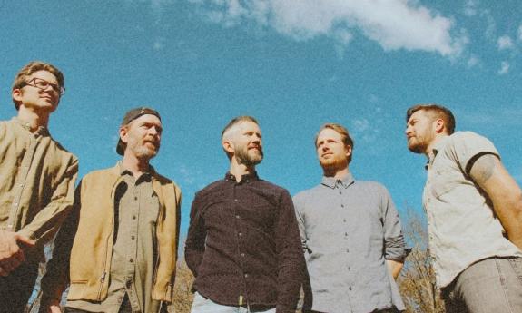 Bandmates from Moon Taxi smile and pose with thick clouds and the sky as their backdrop.