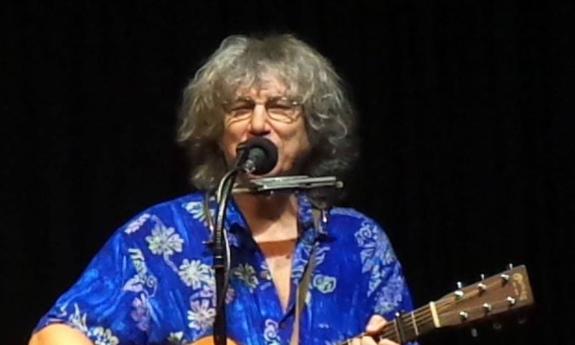 Singer songwriter novelist Rod MacDonald onstage with guitar, smiling