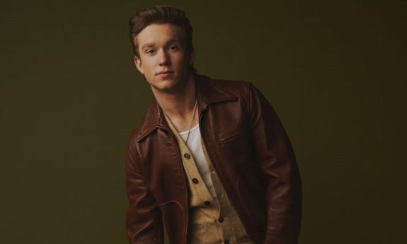 Ty Myers poses in front of a dark green backdrop. 