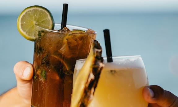 Two cocktails, each held by a hand, with glasses clinking in a toast