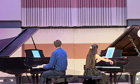 Two grand pianos with open lids, with a pianist performing at each