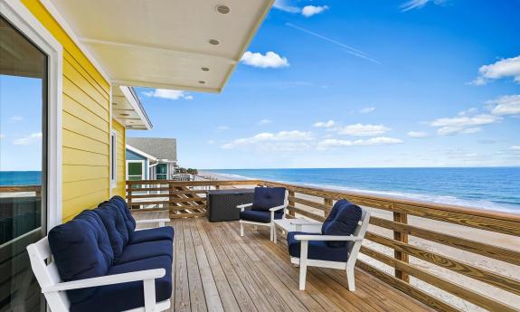 This yellow vacation home on the ocean has blue and white deck furniture