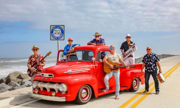 The band Landfall, with instruments, posed around and on an antique red truck near the water on A1A