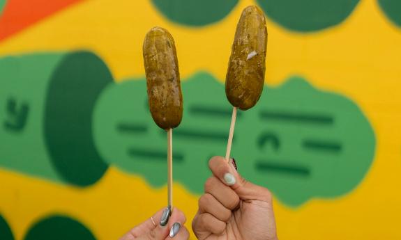 People holding up pickles on a stick