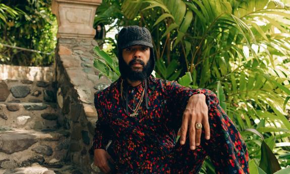 The raggae artist, Protoje, sitting on stone steps surrounded by palms