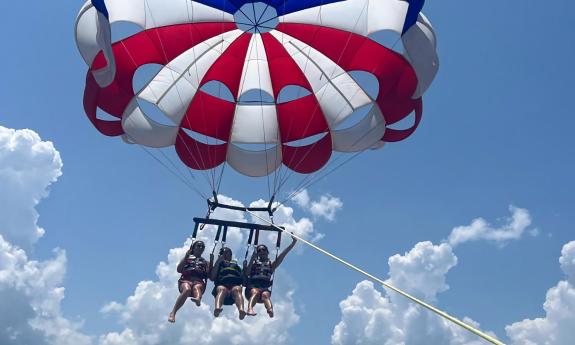 Three young women flying under a red, white, and blue parasail