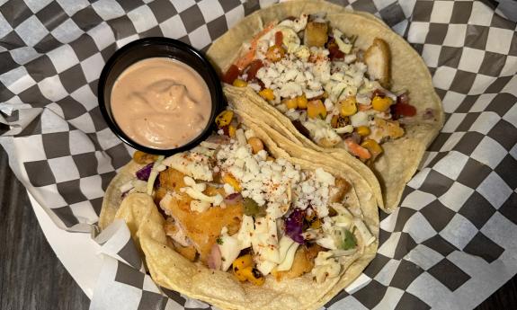 A pair of tacos with a side of sauce