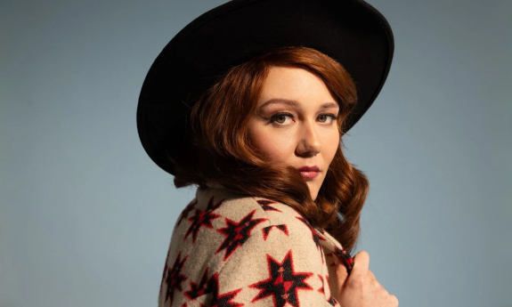 Mary Tuttle dons a black hat and poses in front of a blue backdrop.