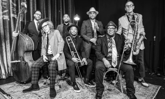Bandmates from Preservation Hall Jazz Band pose in front of an enormous curtain.