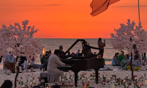 A pianist at a grand piano on a beach at sunset