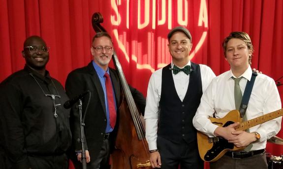 The four musicians in the Raisin Cake Orchestra standing in a studio in front of a red curtain