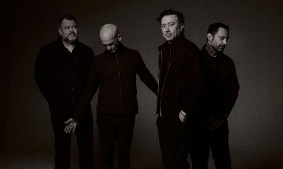 Bandmates from Rise Against wear dark clothing and pose in front of a black backdrop.