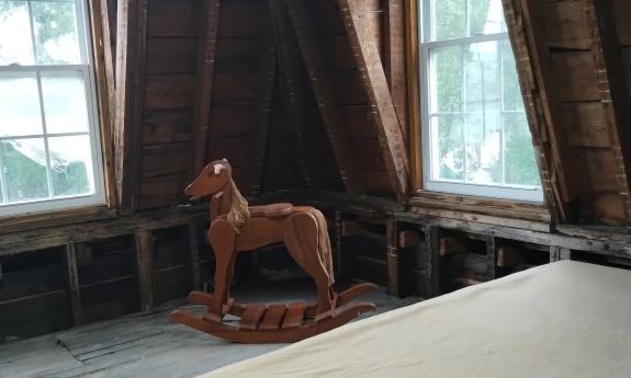 A bare attic, with bed and a small, antique child's rocking horse