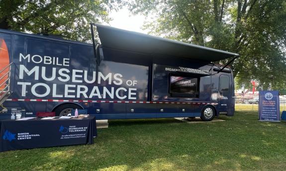 The Mobile Museum of Tolerace, a large blue bus, parked on a tree-covered lawn
