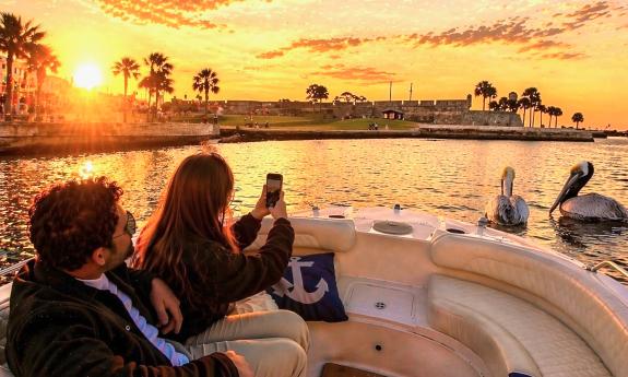Two guests aboard a small charter boat taking photos of pelicans at sunset