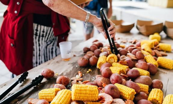 The hands of a woman as she holds tongs to serve the low-country boil