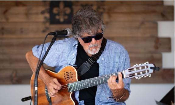 Tony Scozzaro (In dark sunglasses) with his guitar onstage, behind microphone
