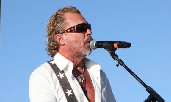 songwriter Jeffrey Steele, onstage singing at microphone, outside
