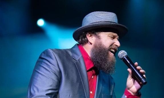 John Nemeth performs on stage in a blue blazer and a matching cap.