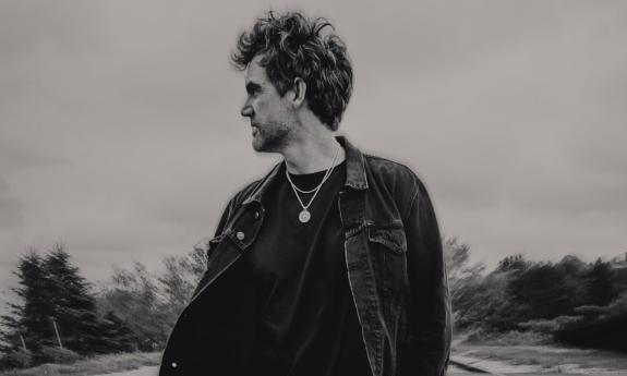 Tyler Hilton wears dark clothing and gazes at an object in the distance.