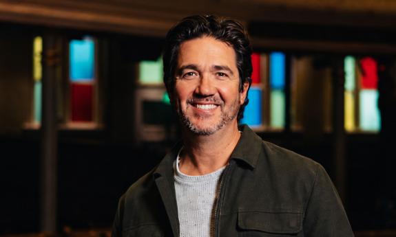 Songwriter Chris Blaire, smiling, with stained glass lights behind