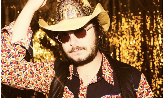 Eddie 9V poses with a cowboy hat, glasses, and a printed shirt with vest.