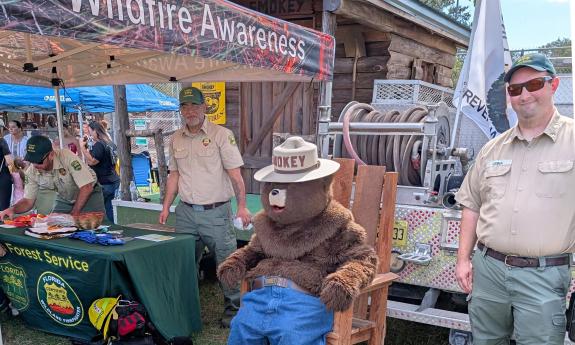 A festival table created by the Forest Service with Smoky sitting in a lawn chair