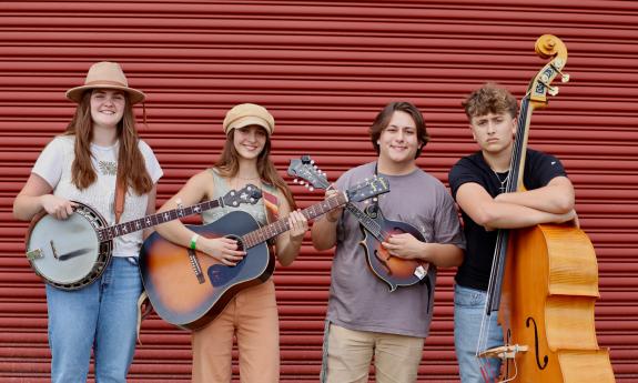 The band Fox Creek standing in front of a red wall, with their instruments