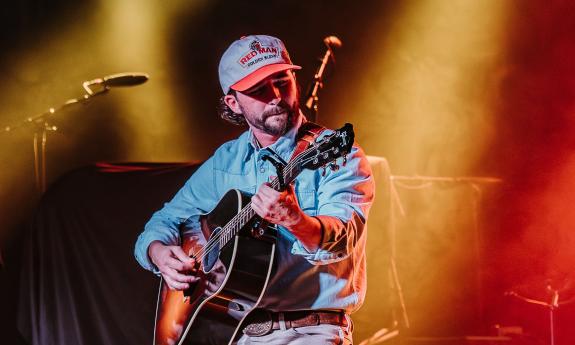 The musician and songwriter Gage Cowart with his guitar on stage under colorful lights