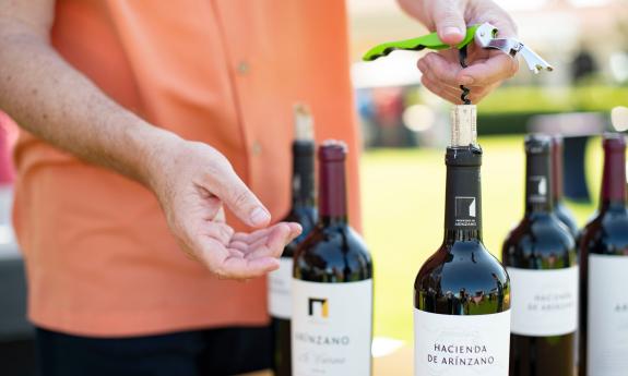 A host opens a bottle of wine for an outdoor tasting