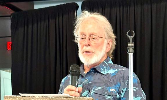 Poet and writer John Stinson at a podium presenting his poetry