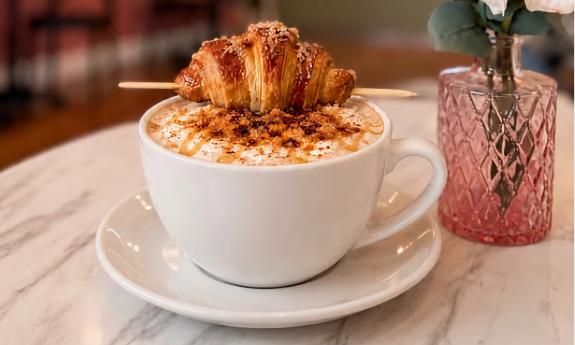 A hot latte with a croissant on top
