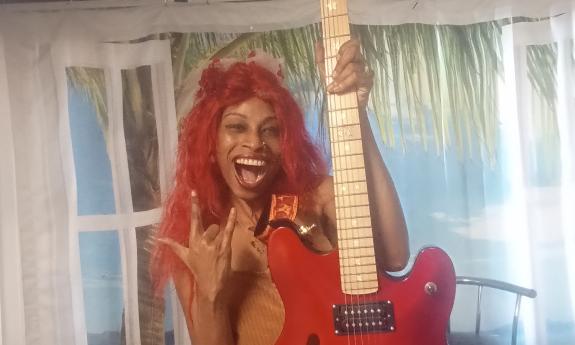 Lydia Flowers against a curtained wall, holding an electric guitar