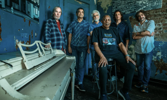 Little Feat huddle together and pose in front of a dark blue backdrop.